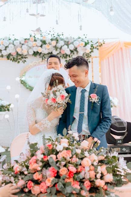 Newlyweds smiling amid lush floral arrangements during a bright wedding ceremony.